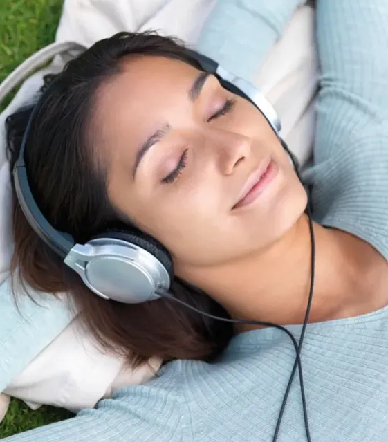 Leende ung kvinna med hörlurar vilar i gräset
